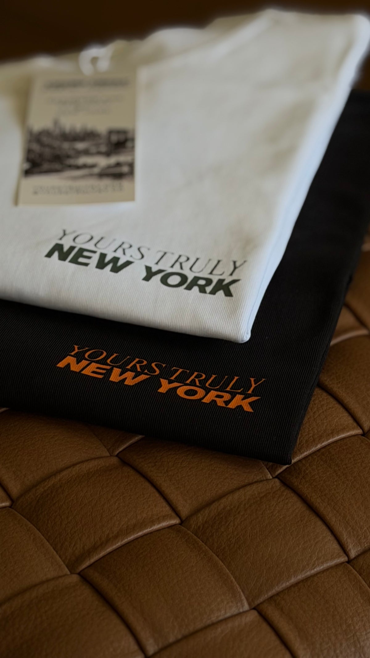 White and black Yours Truly New York tees folded on woven leather